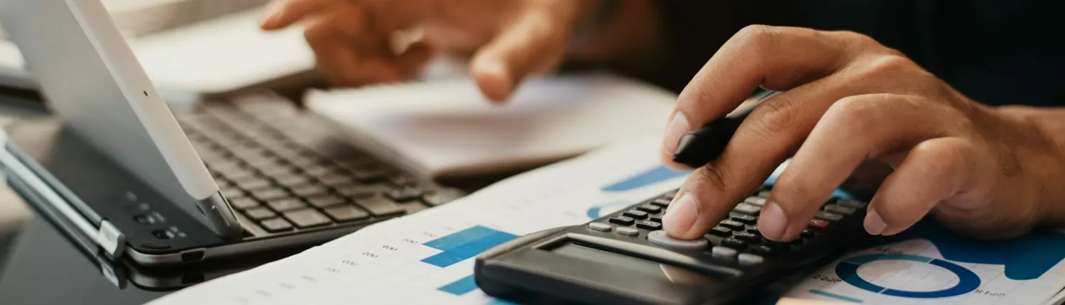 Mains utilisant une calculatrice à côté d’un ordinateur portable