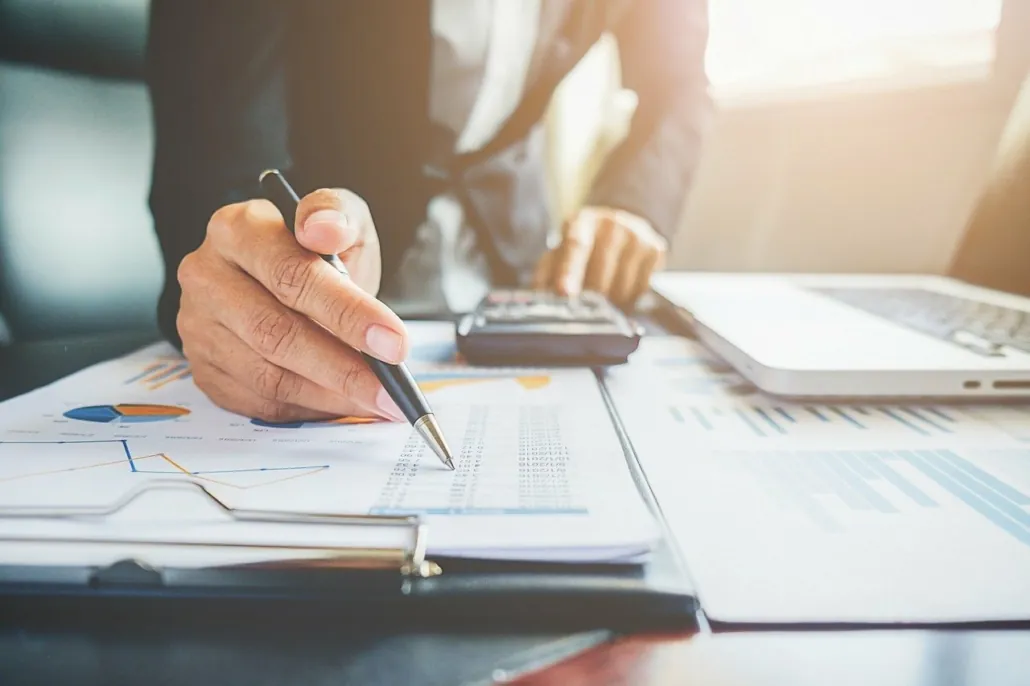 Main tenant un stylo au-dessus de graphiques financiers, près d’une calculatrice